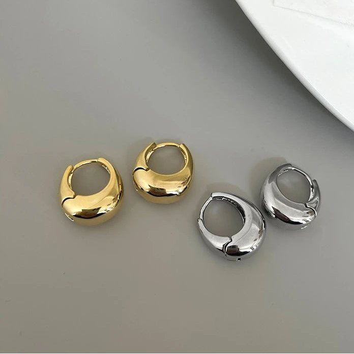 Two gold hoop earrings and two silver hoop earrings on a gray surface with a white plate in the background.